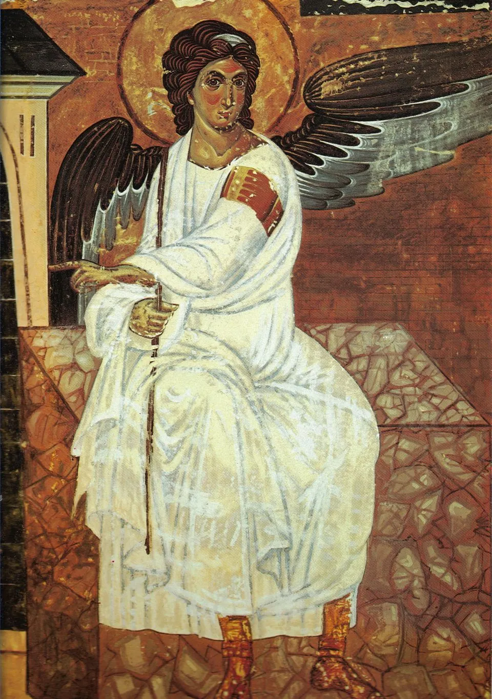 The White Angel of Mileševa: an angel in a white robe with dark wings sits on a stone and points to the side.
